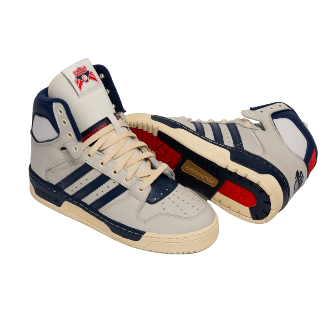 A pair of high-top sneakers in light gray and navy blue with beige laces and soles, featuring red accents on the tongue, heel, and midsole, photographed on a light gray studio background.